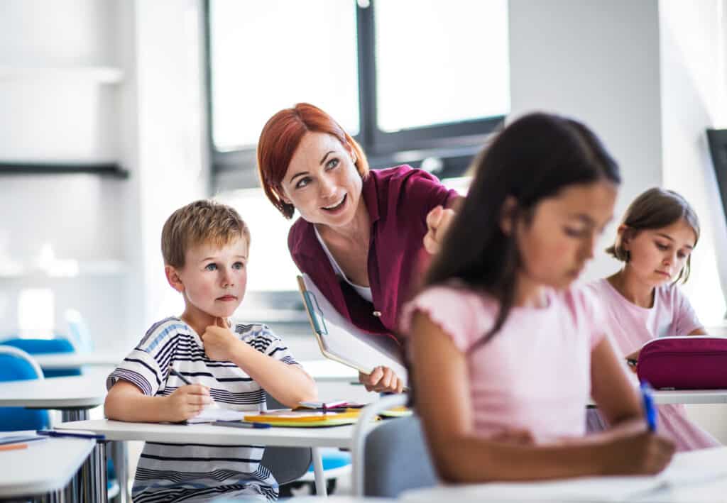 Teacher happiness concept with a happy teacher walking among students on the lesson, explaining and helping.