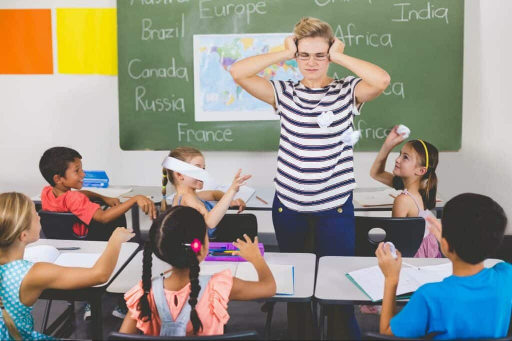 Stressed teacher managing a chaotic classroom filled with energetic students.