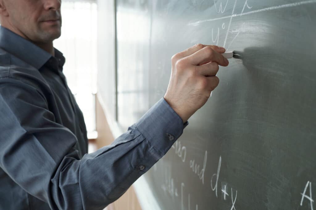 Contemporary teacher with piece of chalk writing formula on blackboard