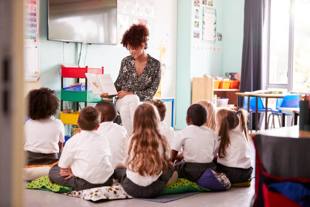 Female Teacher Reading Story To Group Of Elementary Pupils