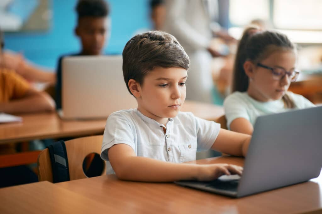 Schoolboy and his classmates studying on laptops while having a class in the classroom.