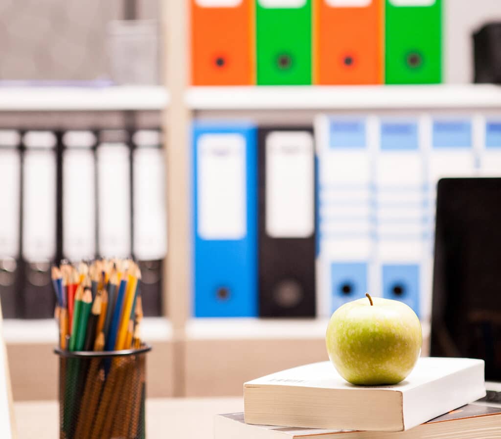 Green apple on pile of books next to a notebook and pencils on the desk