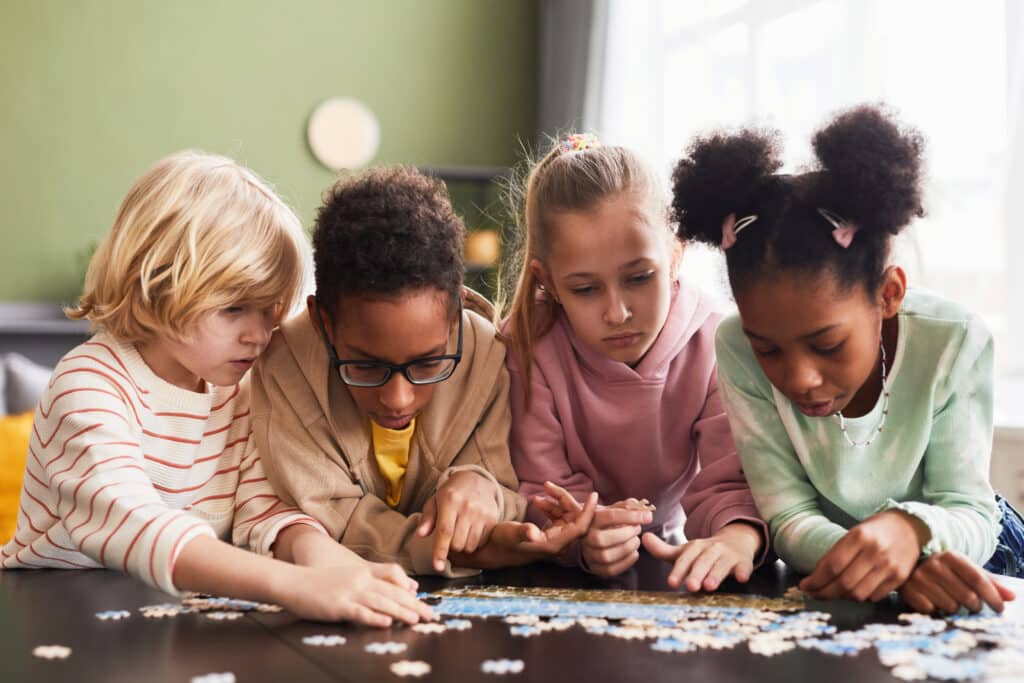 Front view portrait of diverse group of children playing with puzzle game indoors together
