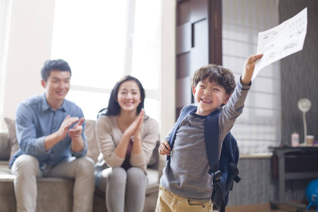 Happy Chinese boy coming home from school with a report card