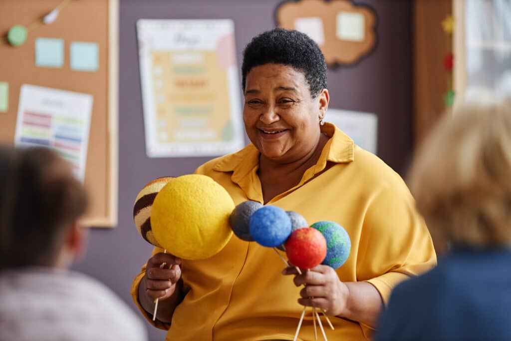 Happy teacher with planet models speaking to classroom