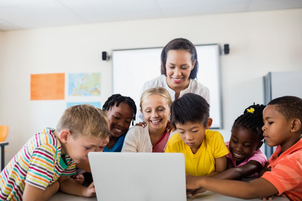 Happy teacher and pupils using laptop in classroom