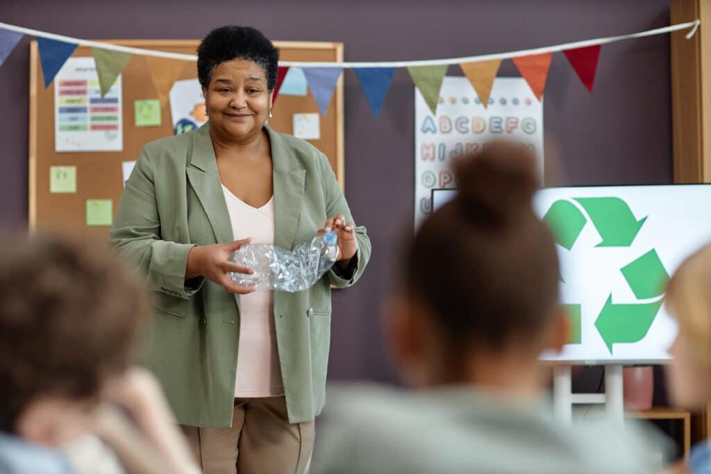 Smiling Black woman teaching little kids about recycling in school