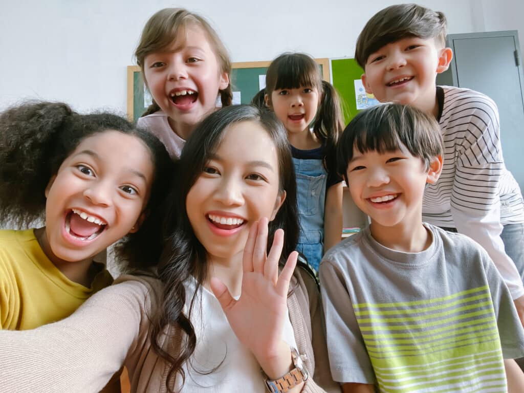 Smiling young Asian teacher making selfie with her class
