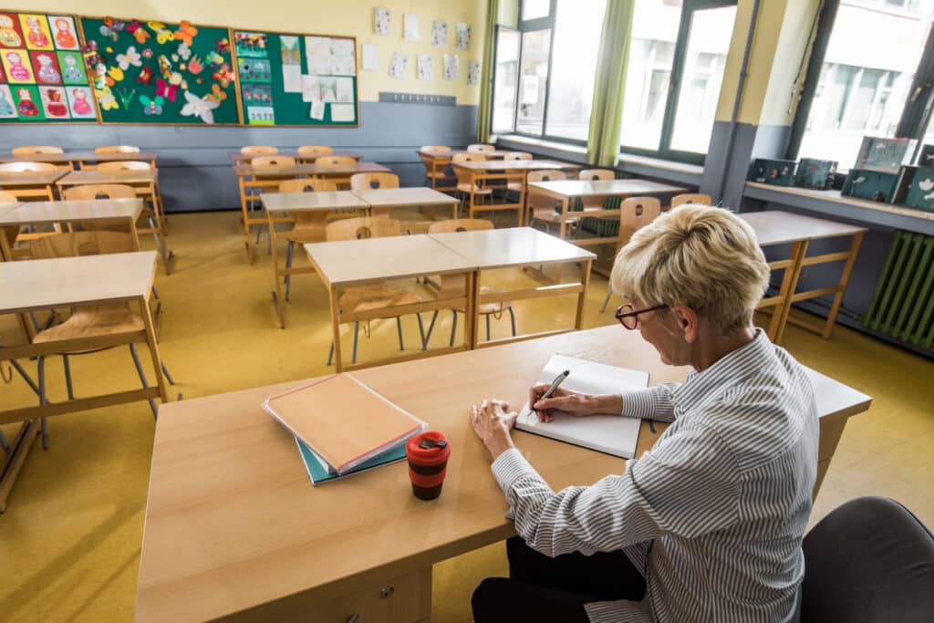 teachers' work hours concept with a teacher at her desk with an empty classroom