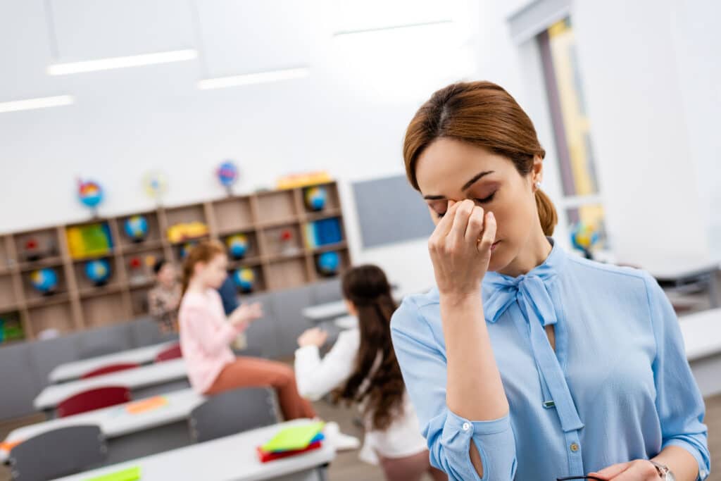 Tired teacher in blue blouse standing in front of desks